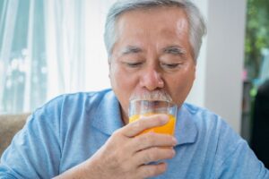 Old man drinking glass of orange juice